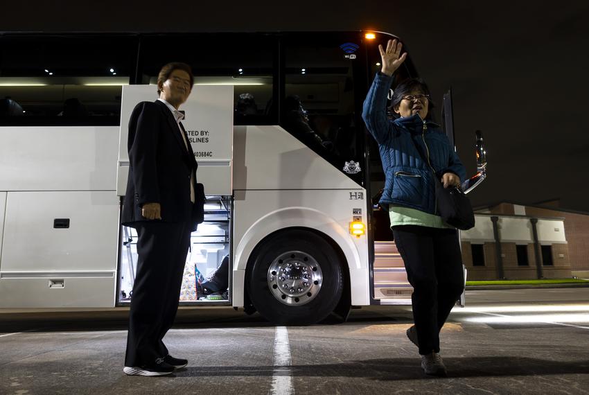 Hyunja Norman waves to people as they arrive at 3:45 a.m. to board a charter bus headed to Austin for a public hearing on Tuesday, April 25, 2023.